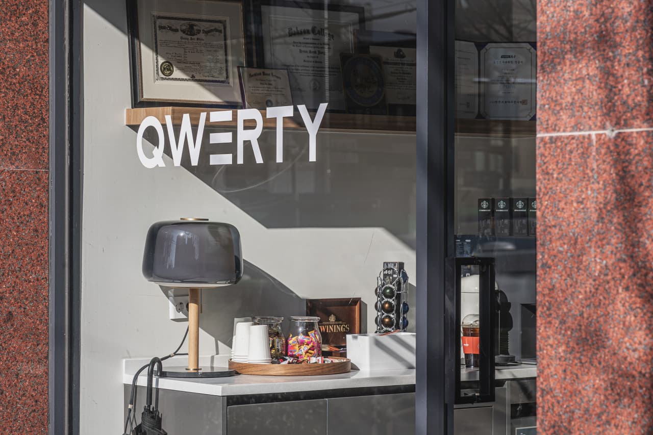 유리에 QWERTY 로고가 비치는 사무실 입구와 리셉션 공간